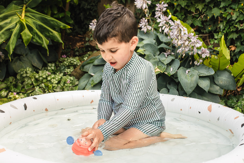 Young child playing with Space Piggy in an outdoor water play setup, smiling and splashing, illustrating the toy's appeal beyond the bath.