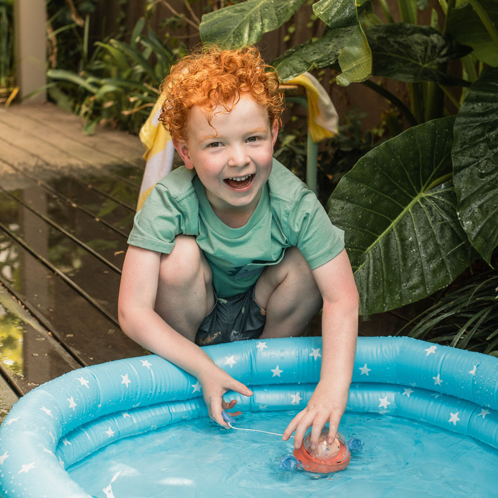 Child sitting beside a tub, watching Space Piggy paddle through water, showcasing cause-and-effect learning through play.