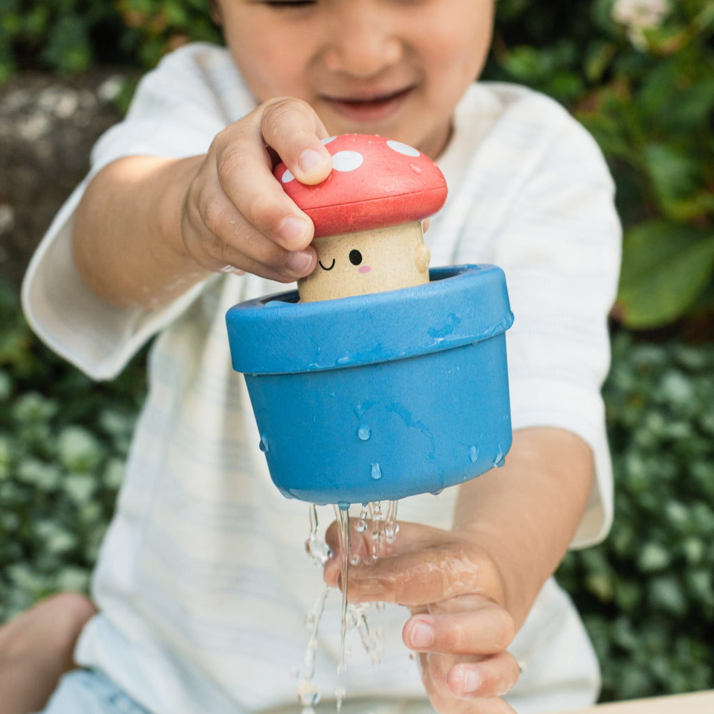 Young child happily holding the mushroom toy outdoors over a water bucket, engaging in interactive water play.
