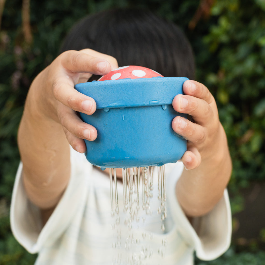 Child lifting the Bath Pop-Up Mushroom over their head, showing water trickling down and engaging in active bath-style fun outdoors.