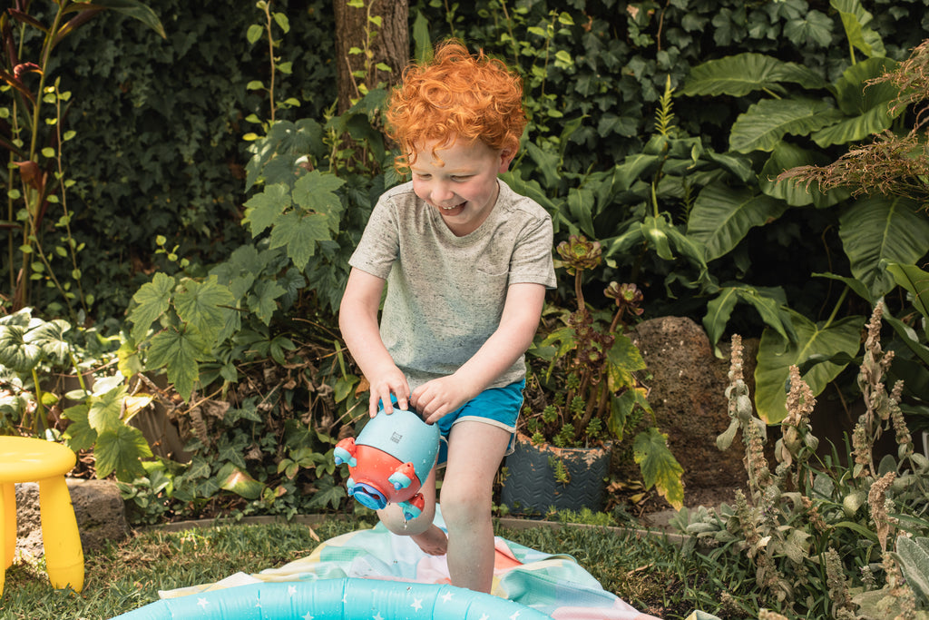 Young child with wet hair and a joyful expression holding the Bath Rocket outdoors, illustrating real-life fun and sensory delight.
