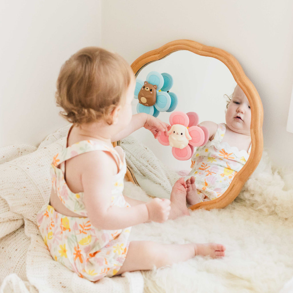 Baby sitting on a rug playing with the pink Bunny Sensory Spinner stuck to a mirror, engaging in interactive, fine motor sensory play.