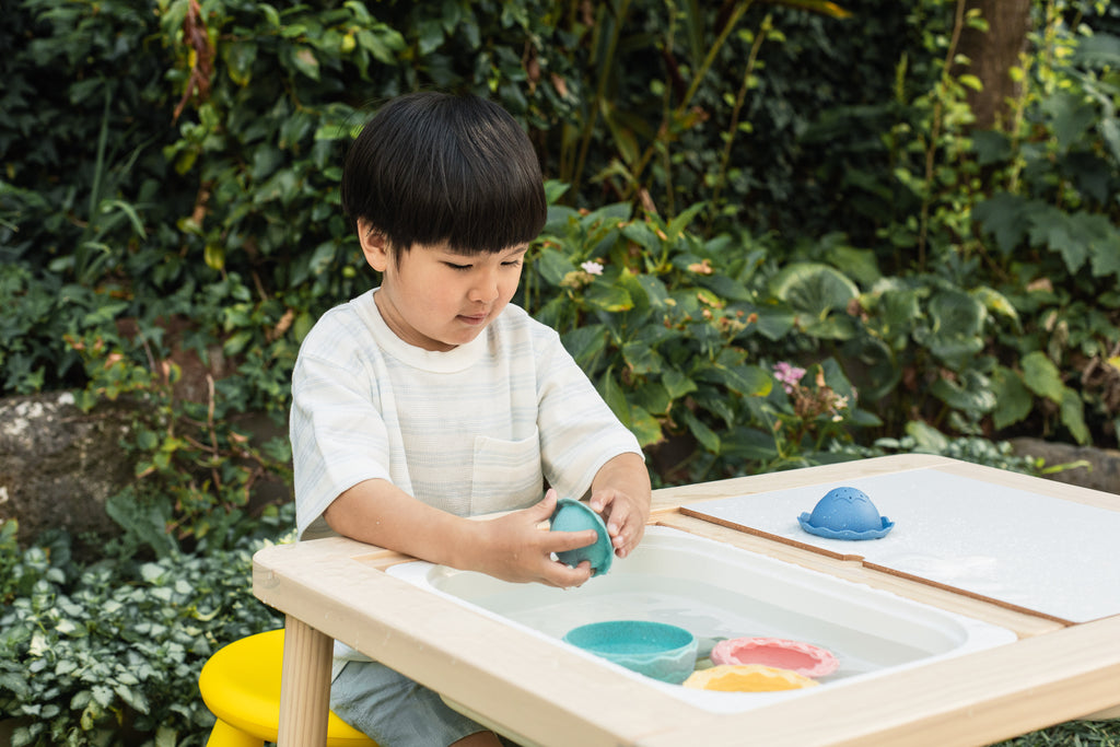Child separating and exploring the egg cups on a play table, demonstrating cognitive play and colour sorting skills.