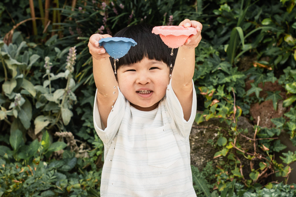 Smiling child holding Bath Egg high, water sprinkling below as they playfully engage with the toy’s sensory and motor skill-boosting features.