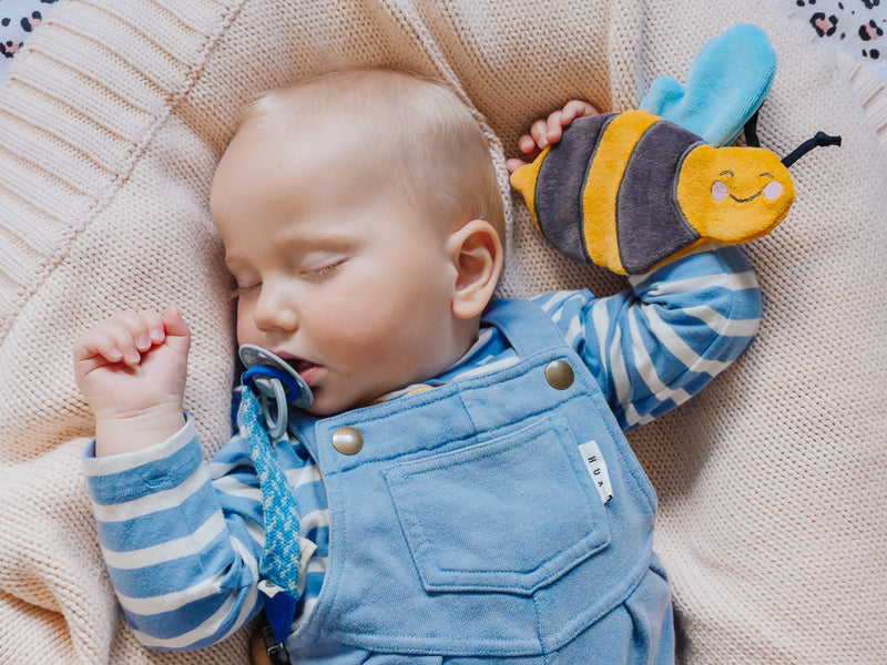 Newborn baby lying on a soft surface with eyes closed, gently grasping the bee scrunchie toy, illustrating calm and sensory engagement.