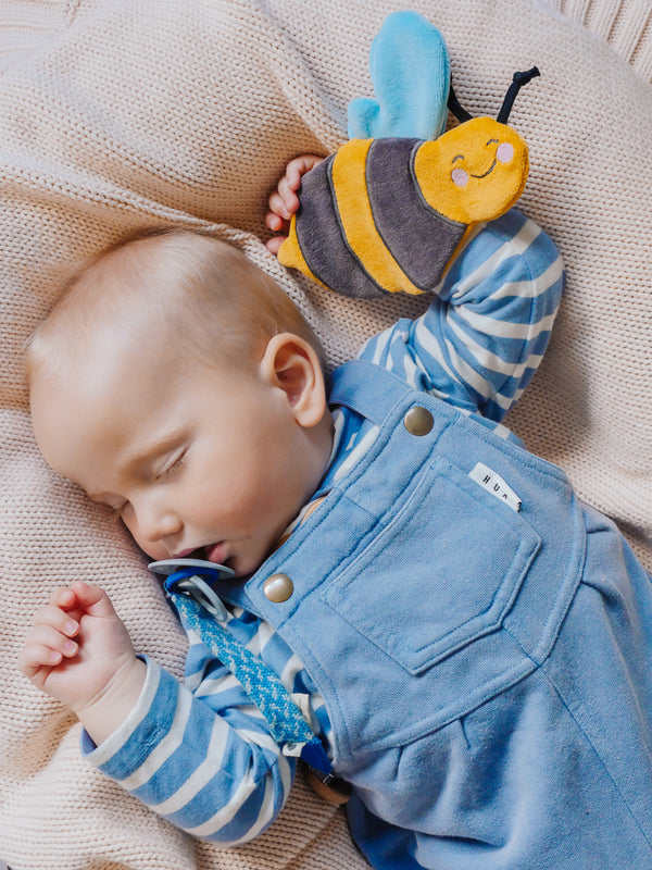 Baby in a blue outfit holding and exploring the crinkle bee scrunchie toy, showcasing interactive, sensory play for early development.
