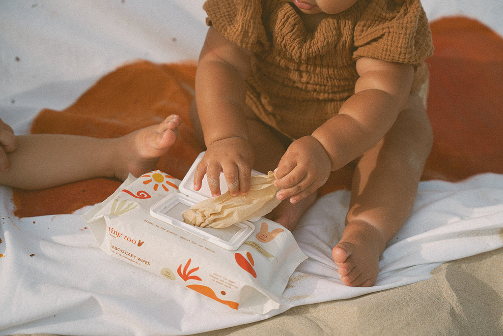 Infant gently pullinh out Tiny Roo bamboo baby wipes from packet, showcasing soft, dermatologist-approved wipes perfect for sensitive baby skin.