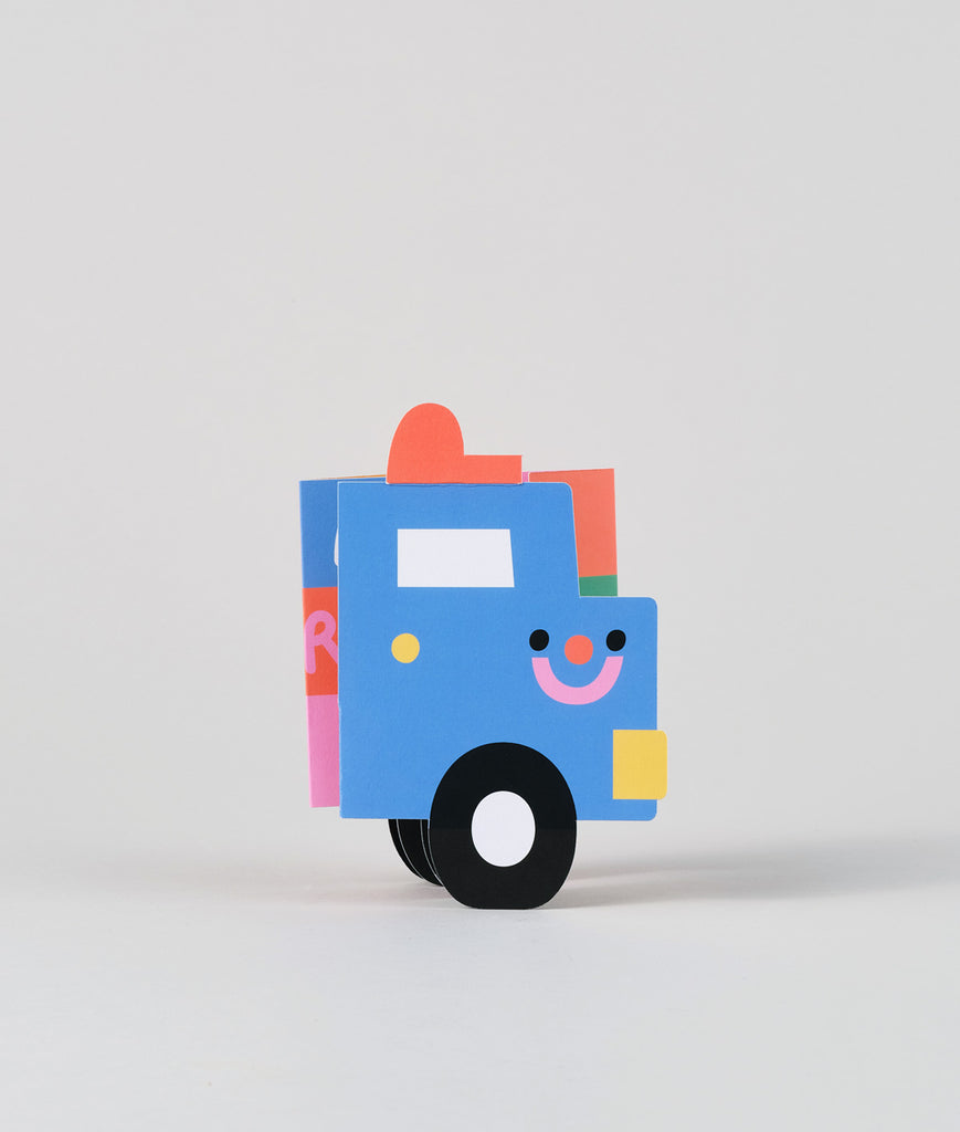 Truck-shaped birthday card standing upright with a wide grin, showing off its bright design and geometric shape.