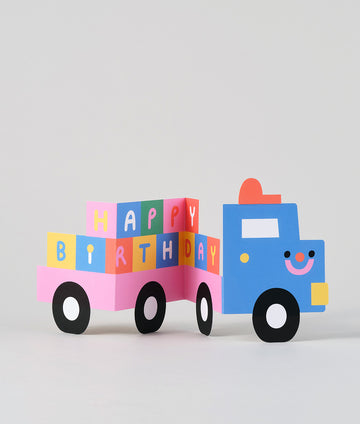 Fold-out birthday card shaped like a blue truck carrying colourful blocks spelling “HAPPY BIRTHDAY” across the trailer.
