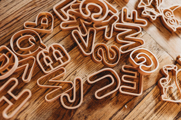 Top view of eco-friendly alphabet cutters arranged on a wooden surface, made from recycled sawdust and PLA plastic.