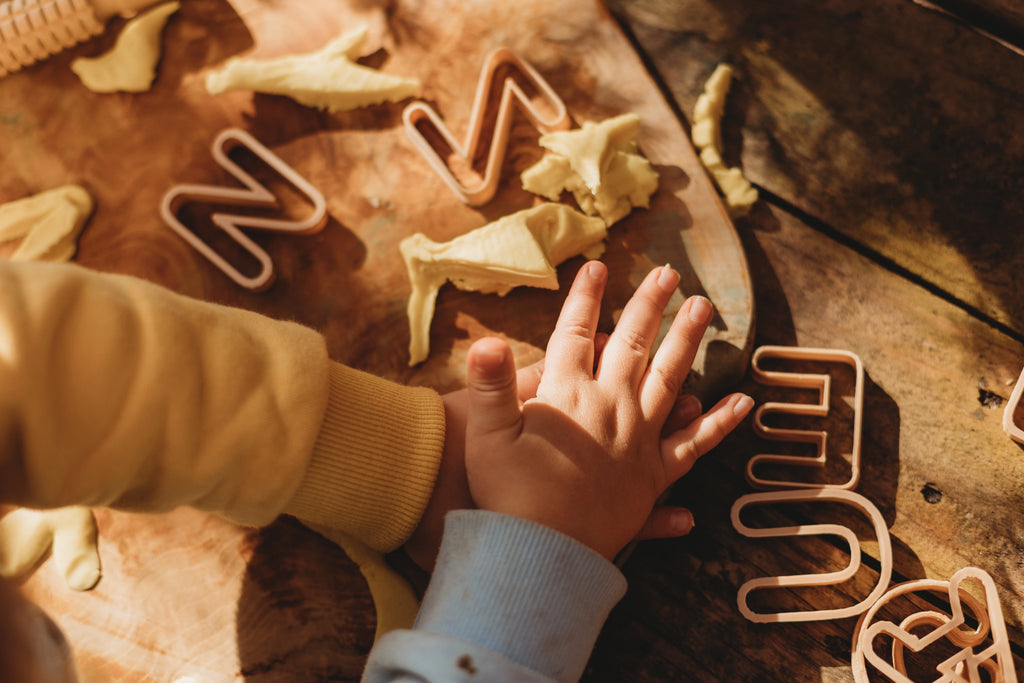 Child playing with alphabet cutters and playdough on a table.