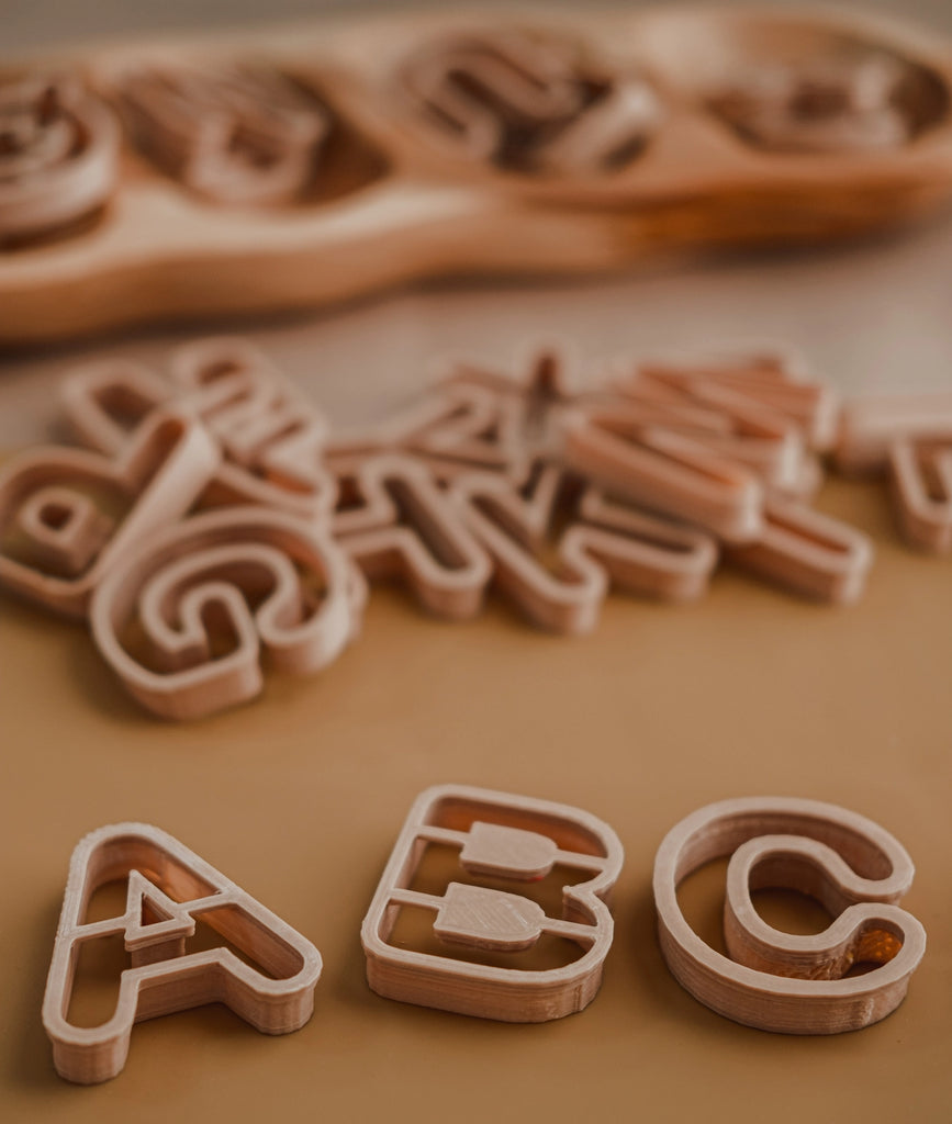 Eco letter-shaped playdough cutters on a wooden surface