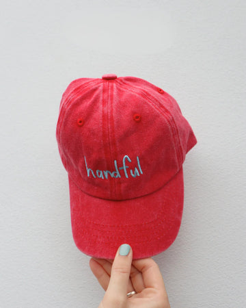 Front view of the watermelon red "Handful" kids cap featuring colourful embroidered text and soft, washed cotton—perfect for playful little personalities.