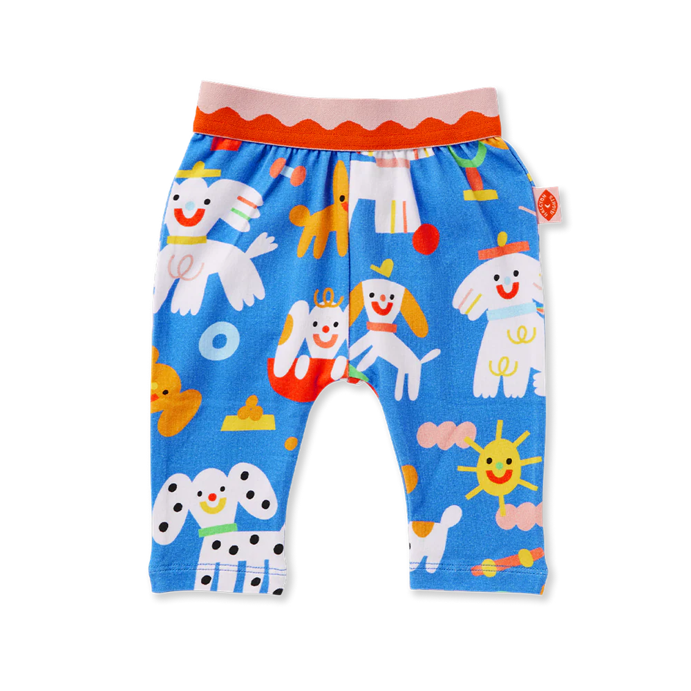 Flat lay of Halcyon Nights Puppy Park Baby Leggings featuring bright blue fabric with playful multicoloured dog, sun, and toy illustrations, plus a pink and red elastic waistband.