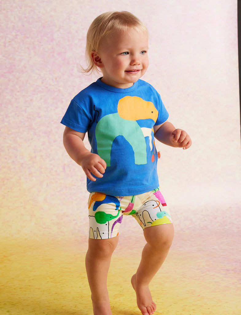 Side profile of toddler wearing Happy Herd Bike Shorts and matching blue t-shirt, smiling and posing confidently against a pastel backdrop.