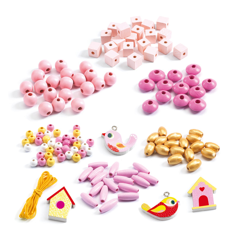 Flat lay of Djeco bead set contents including pink, white, and gold wooden beads, bird and birdhouse charms, and yellow threading cord.