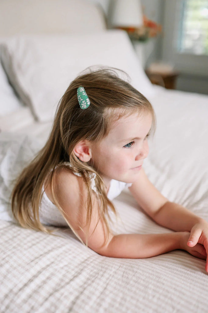 Young girl lying on a bed with a green hair clip in her hair