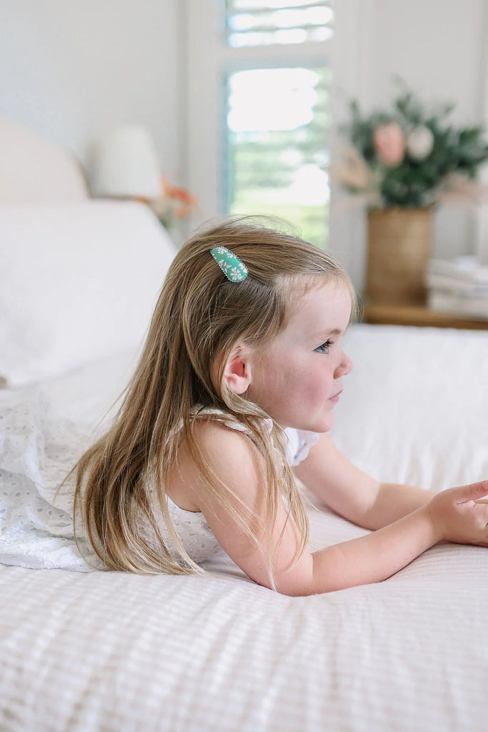 Young girl lying on a bed with a floral headband, looking out a window.