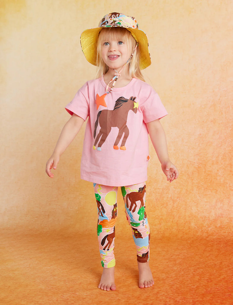 Child smiling in Giddy Up Kids Leggings and matching tee with playful horse graphics, paired with a printed bucket hat.