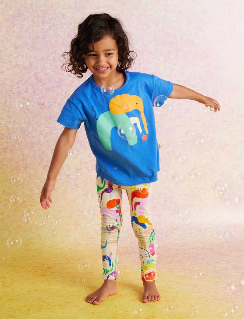 Child wearing Happy Herd Kids Leggings and a blue elephant tee, twirling and smiling against a pastel pink and yellow background.