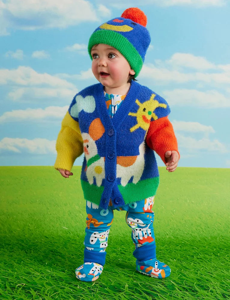 Baby in colourful knit cardigan and Halcyon Nights Puppy Park baby leggings, standing on green grass with a bright blue sky background, smiling with excitement.