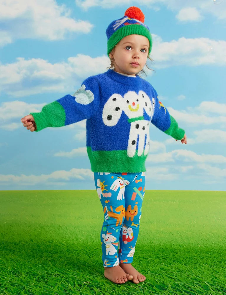 Toddler wearing Puppy Park baby leggings and blue dog-themed knit jumper, arms stretched out while standing barefoot on green grass with a sky backdrop.