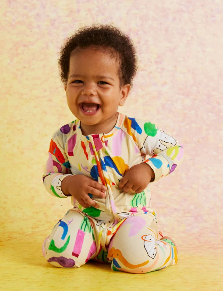 Smiling baby wearing the Halcyon Nights Happy Herd romper, sitting against a yellow background, showcasing full-body fit and vibrant design.