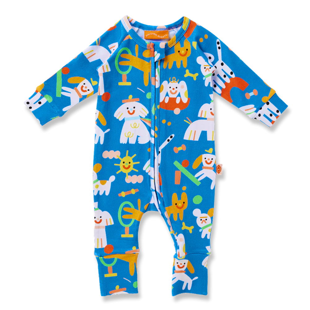 Halcyon Nights Puppy Park Long Sleeve Romper flat lay showing colourful illustrated puppies, toys, and suns on a bright blue background.