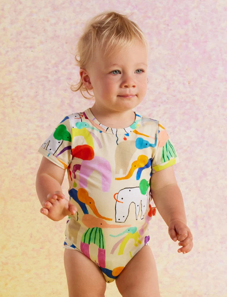 Baby walking in the Halcyon Nights Happy Herd bodysuit, surrounded by a soft pastel background, highlighting the vibrant design and comfy fit.
